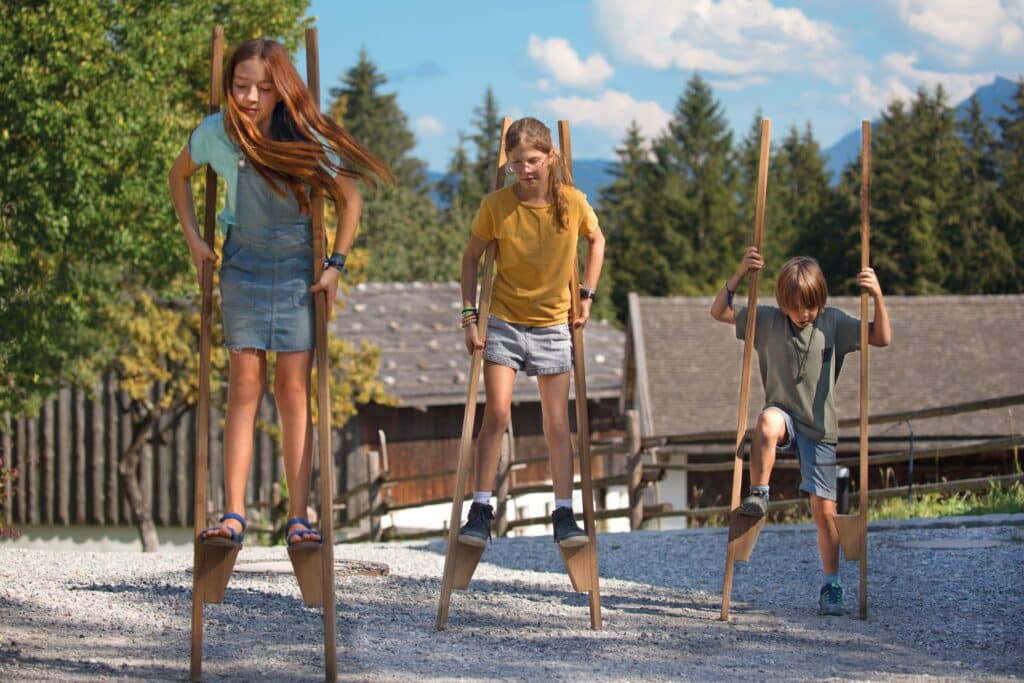 Drei Kinder laufen auf Stelzen.