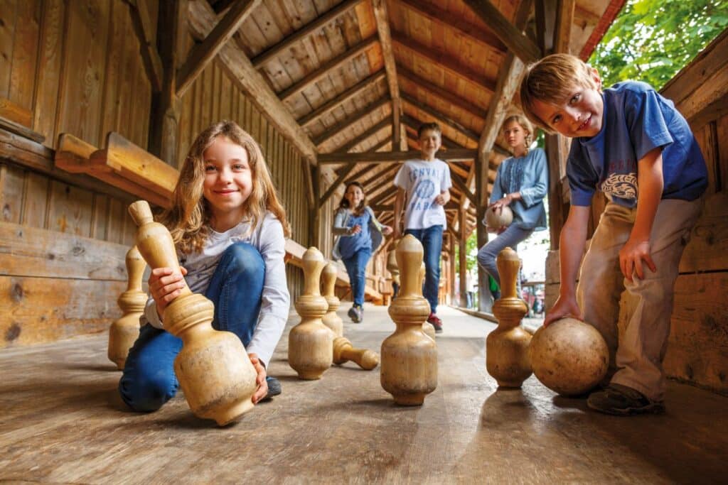 Kinder spielen in einer historischen Kegelbahn.