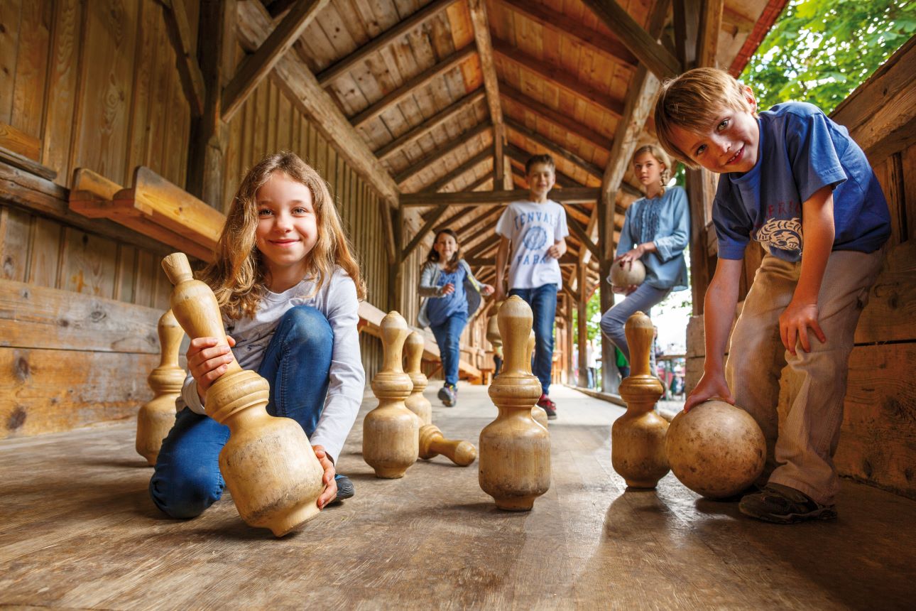 Kinder spielen in einer historischen Kegelbahn.