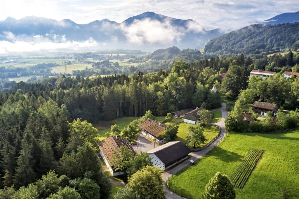 Vogelperspektive auf einen historischen Bauernhof vor Bergpanorama