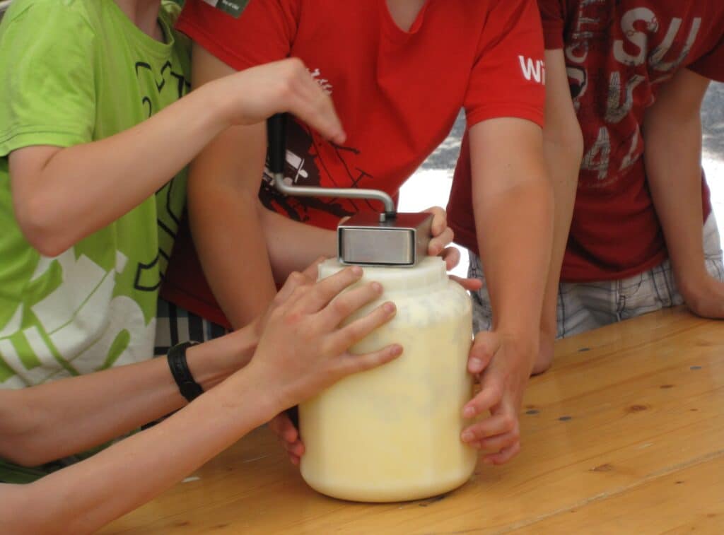Kinder buttern mit einem handbetriebenen Butterrührgerät.
