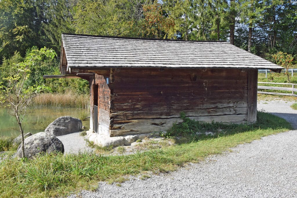 Eine mit Holzschindeln gedeckte kleine Hütte am Ufer eines Gewässers.