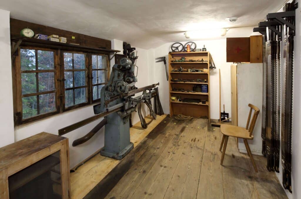 In einem Raum hängen rechts lange Sägeblätter, links befindet sich ein Fenster, davor ein altes Gerät.