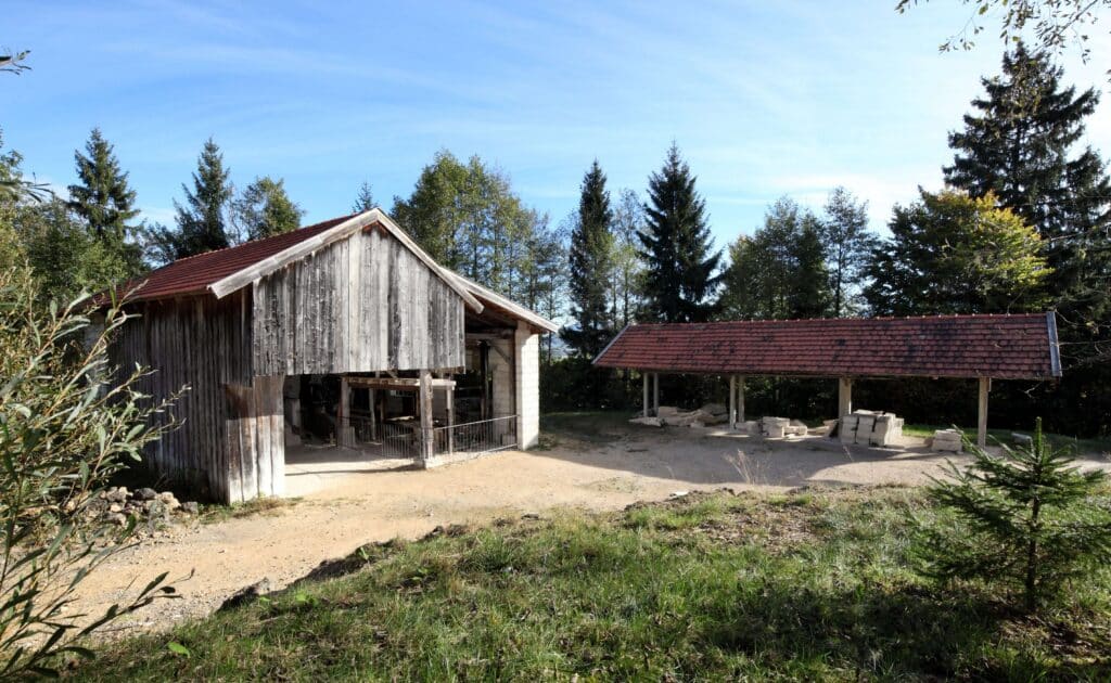 Zwei Gewerbegebäude: eine Werkstatt und ein überdachter Lagerplatz. Dort liegen Steine.