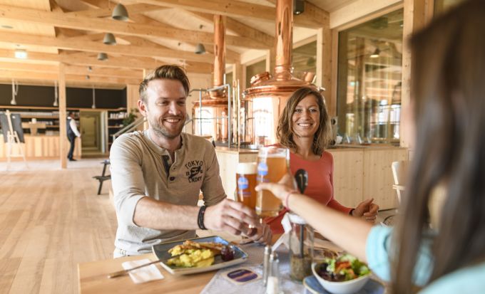 Drei Menschen sitezn an einem Tisch im Wirtshaus und prosten sich zu