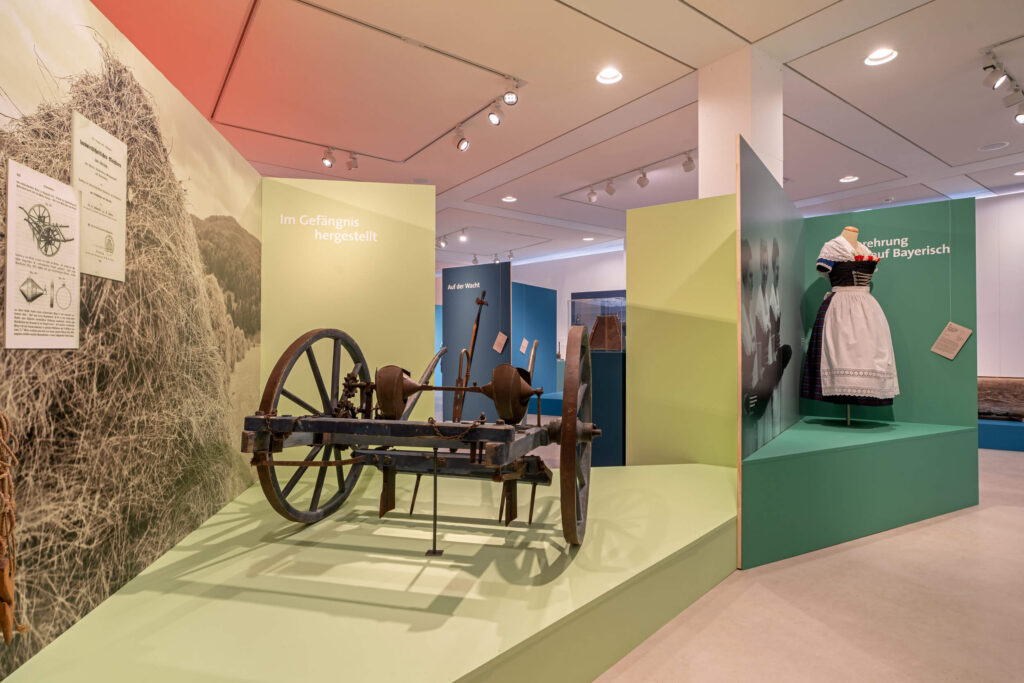 Auf einem hellgrün gestrichenen Podest befindet sich eine historische Sämaschine, rechts daneben auf einem dunkelgrün gestrichenen Podest ein Dirndl.